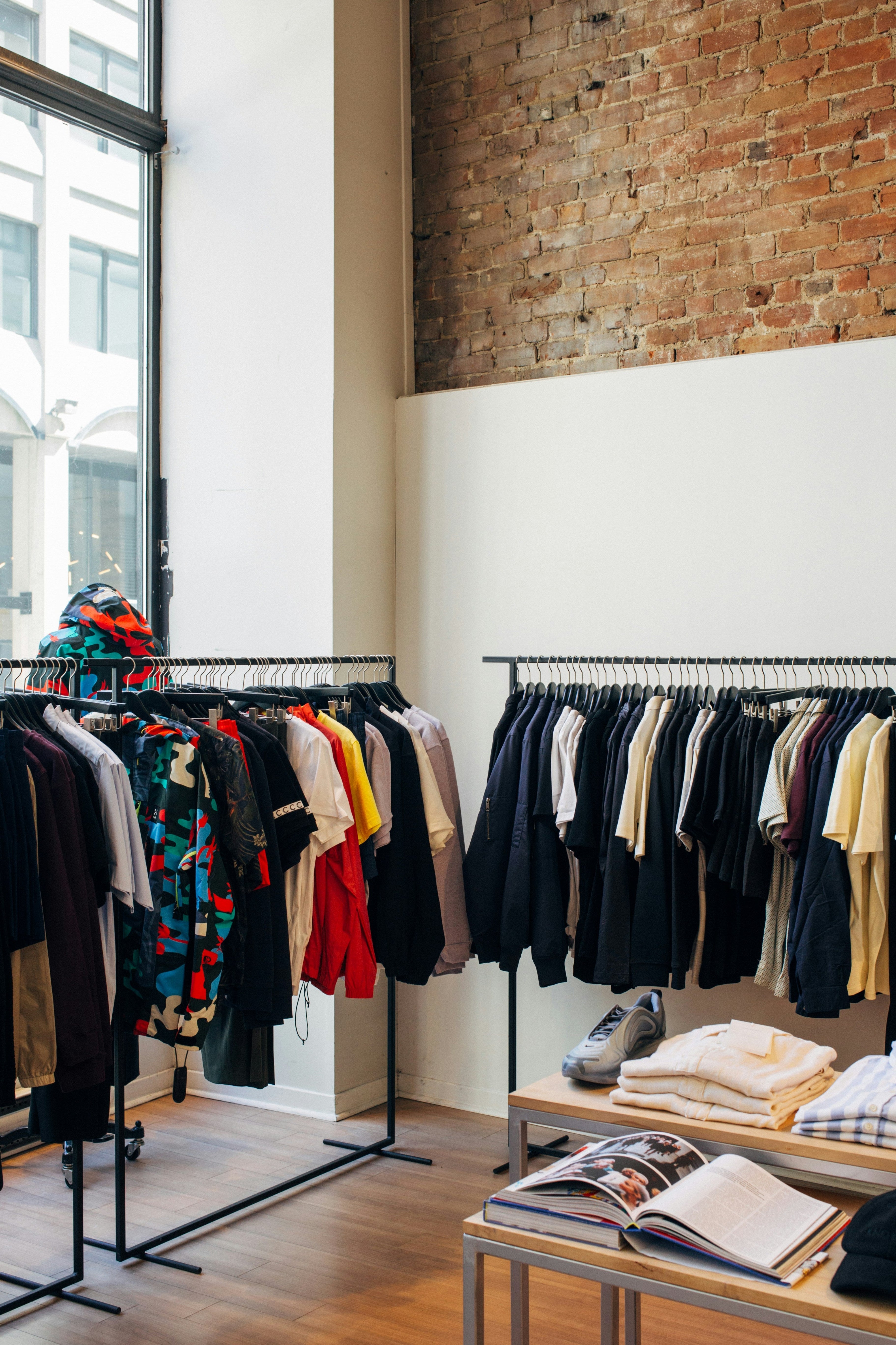 Clothing store interior with racks of clothes and a brick wall.